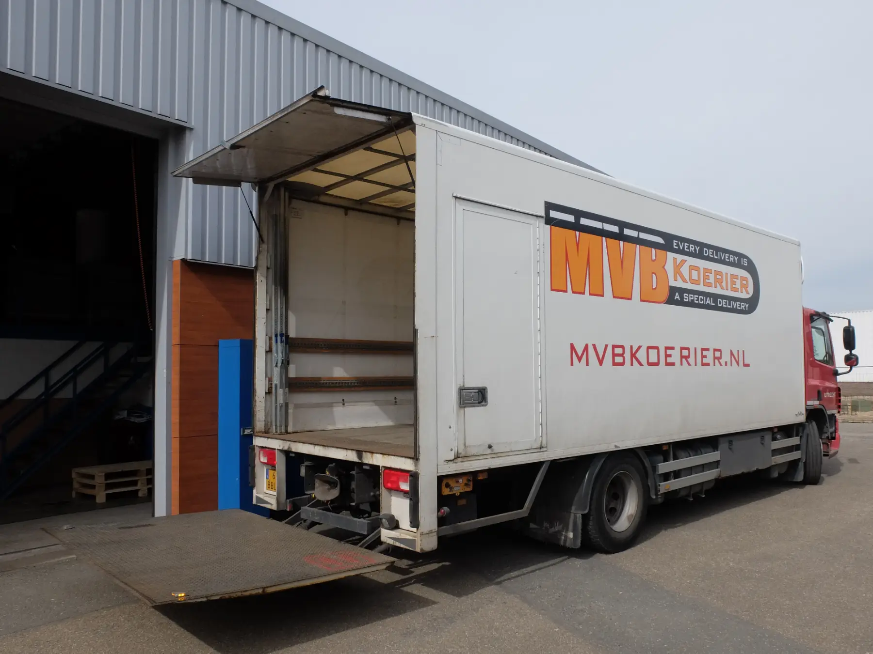 MVB Koerier bakwagen met open laadklep bij een bedrijfspand